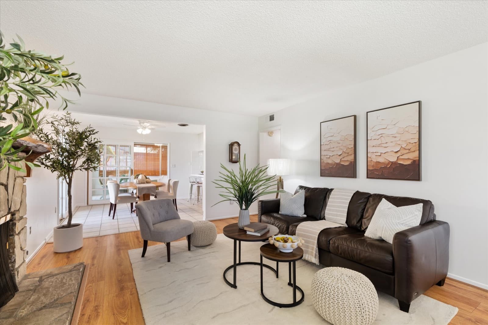 Living room with a brown leather sofa, stone fireplace, light wood floors, and a pair of framed abstract prints, opening toward the dining area