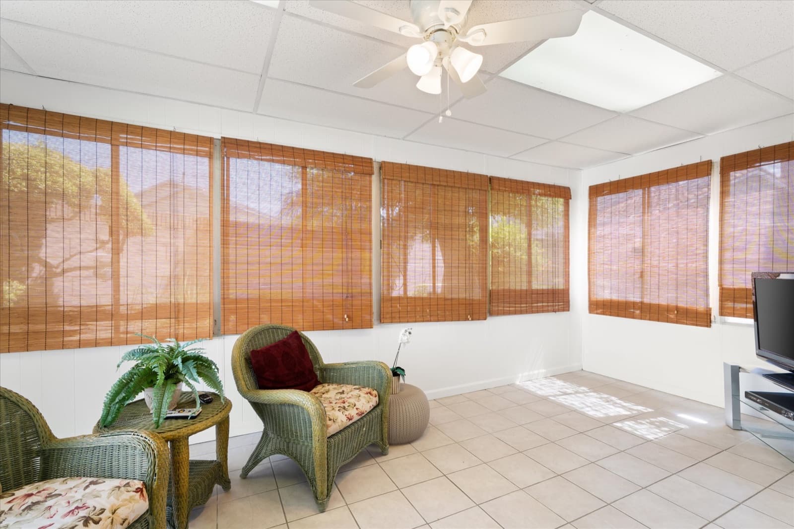 Enclosed sunroom with wicker seating, tile flooring, and bamboo roller shades across a wall of windows