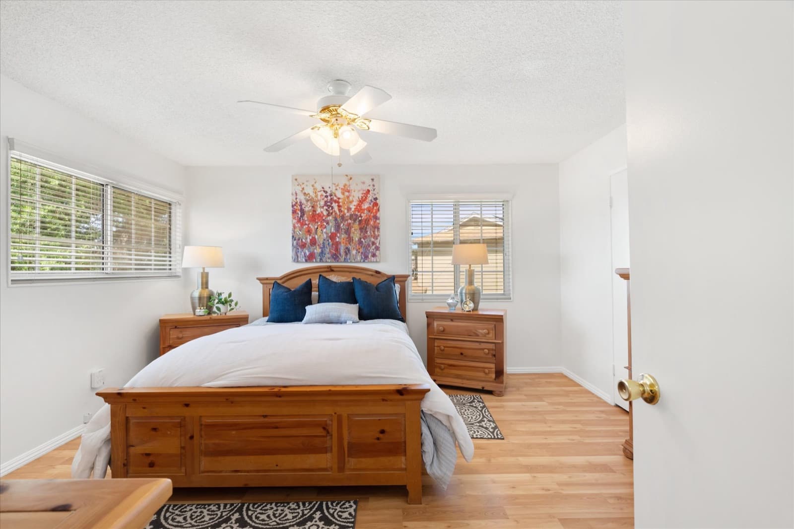 Primary bedroom with a pine bed frame, matching nightstands, two windows, and a ceiling fan
