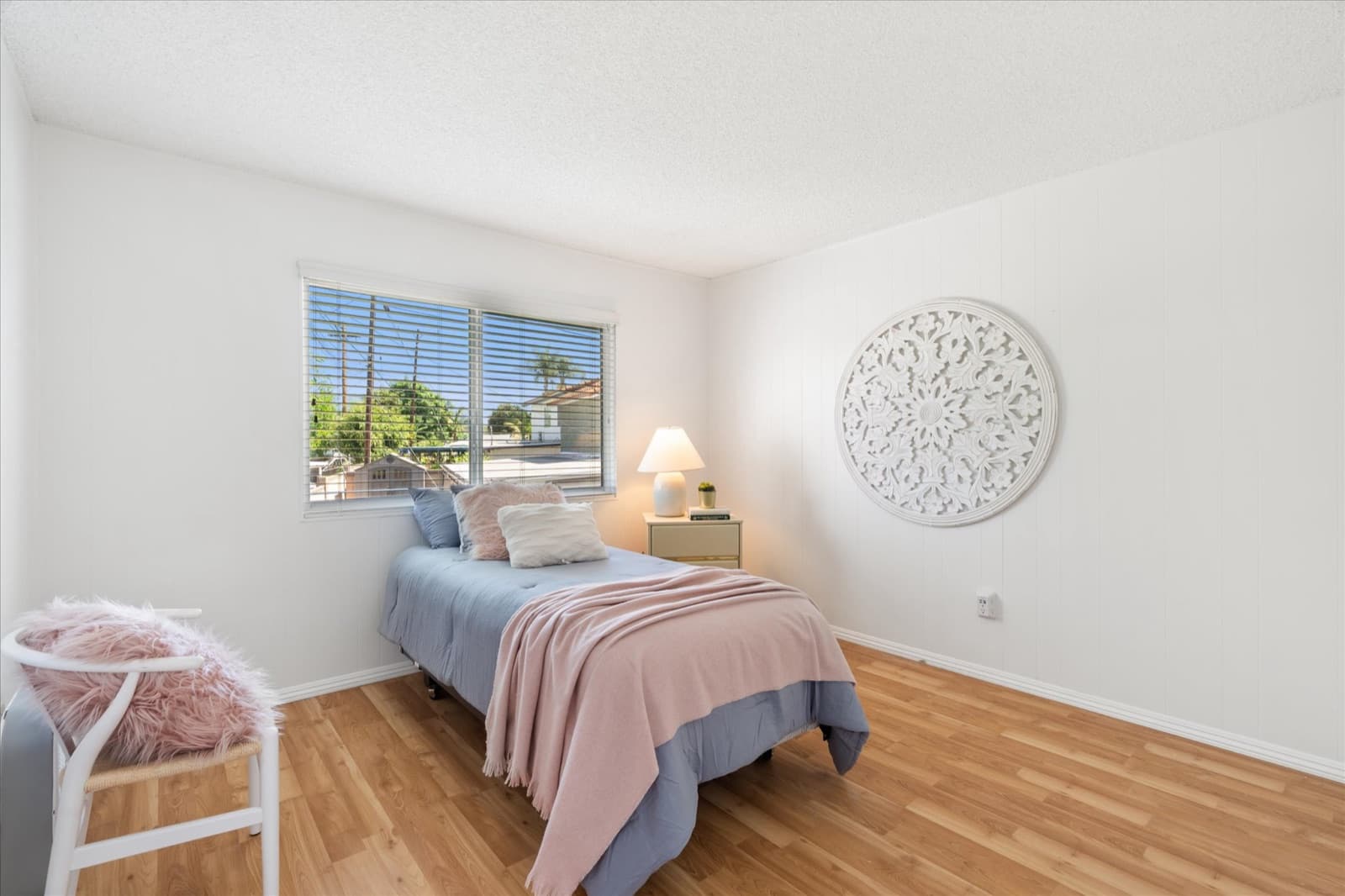 Secondary bedroom with a twin bed, a carved white round wall medallion, and a window looking out to palm trees