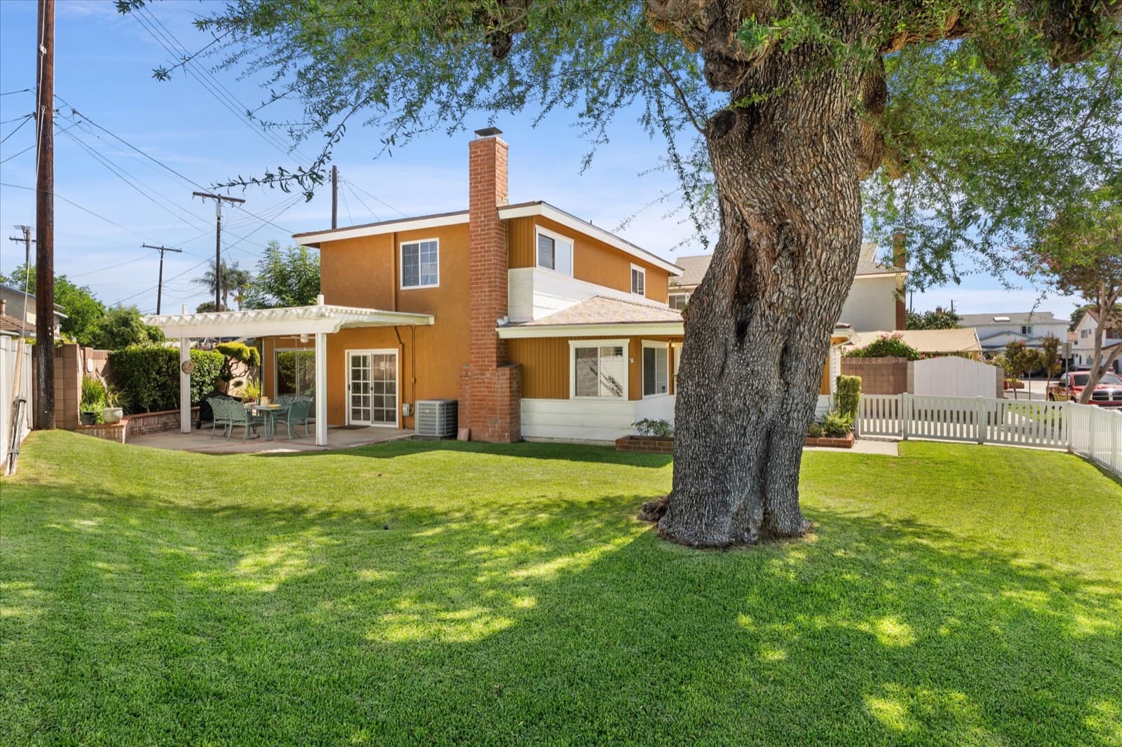 Backyard lawn with a mature shade tree, the home's rear elevation, and a covered patio along the back of the house