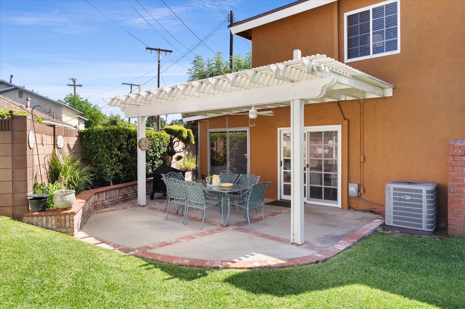 Covered patio with a white lattice patio cover, brick-edged concrete, and a patio table and chairs beside sliding glass doors