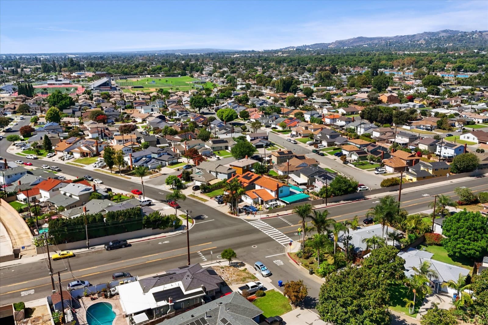 Wide aerial view of South Whittier showing a main cross street, surrounding homes, and a school athletic field in the distance