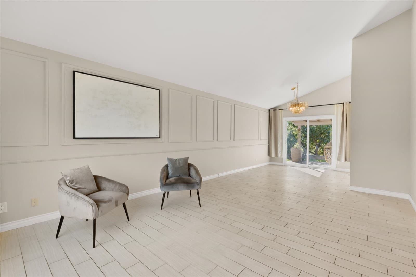 Wide living room with decorative wall paneling, a vaulted ceiling, and sliding doors to the backyard