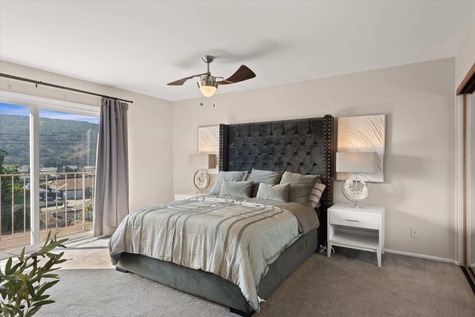 Primary bedroom with a tufted headboard, ceiling fan, and a sliding door onto a balcony with foothill views