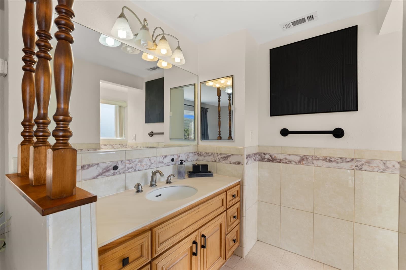 Primary bathroom with a wood vanity, a large mirror, and marble-patterned tile surround
