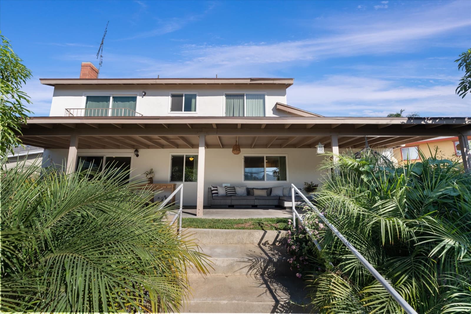Rear exterior of the home with a full-width covered patio, steps, and landscaped backyard planting