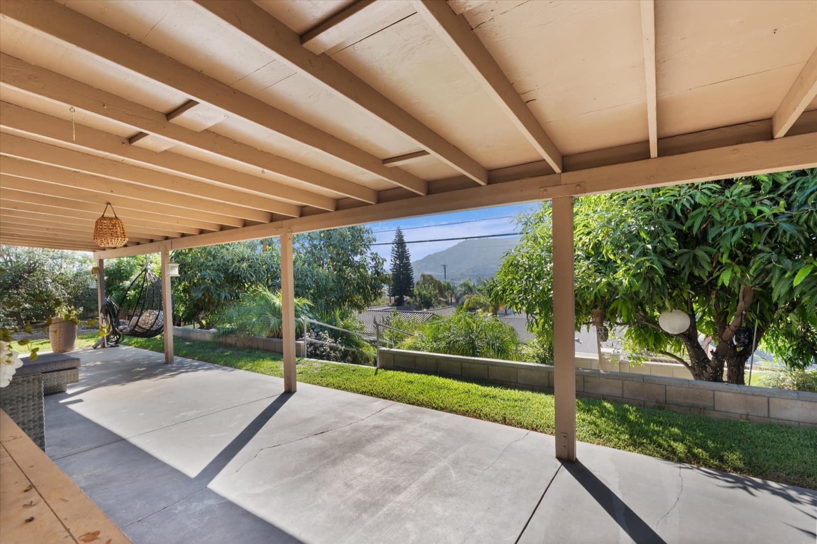 Covered backyard patio with an open-beam roof looking out to the garden and hillsides