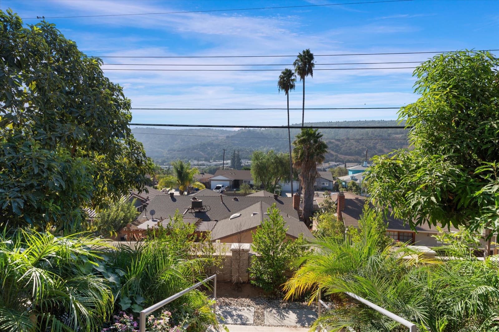 Backyard view over neighboring rooftops and palm trees toward the Whittier foothills